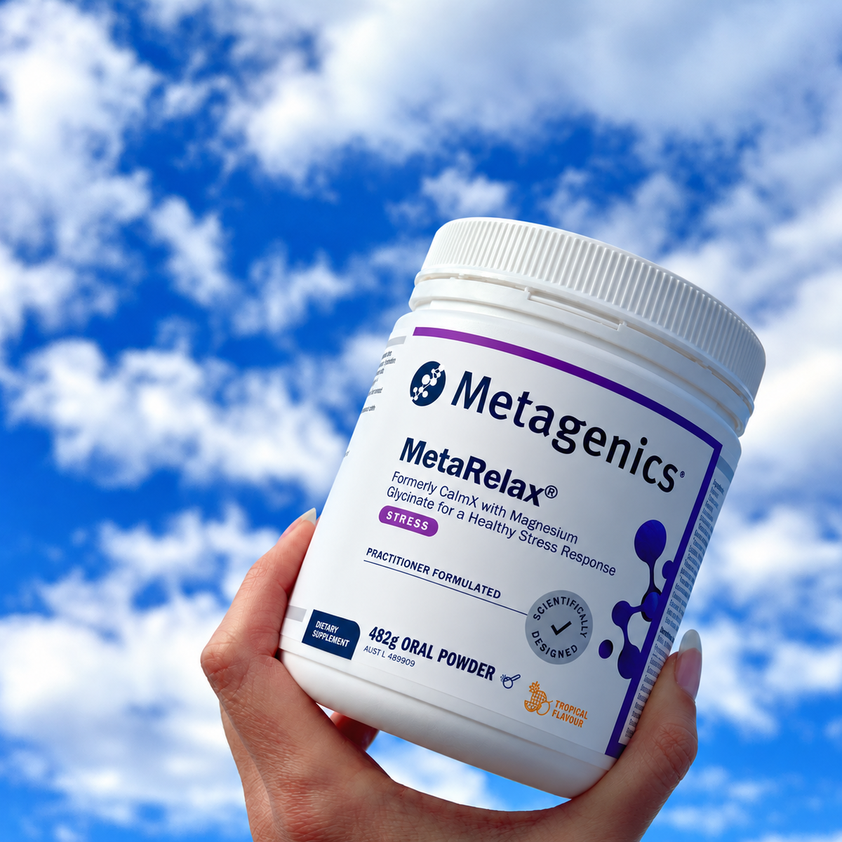 Metagenics MetaRelax Tropical 482g held against a blue sky